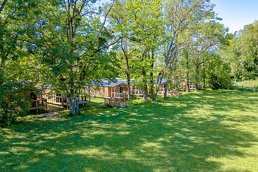Row of wooden Mobile Homes with shaded terraces at CLICOCHIC Aloua campsite in Sevrier (74).