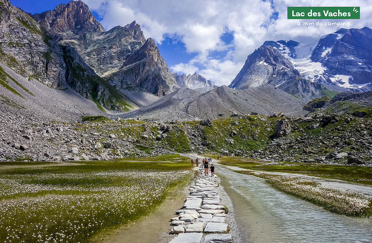 Stone path crossing Lac des Vaches, majestic alpine mountains, Pralognan la Vanoise.
