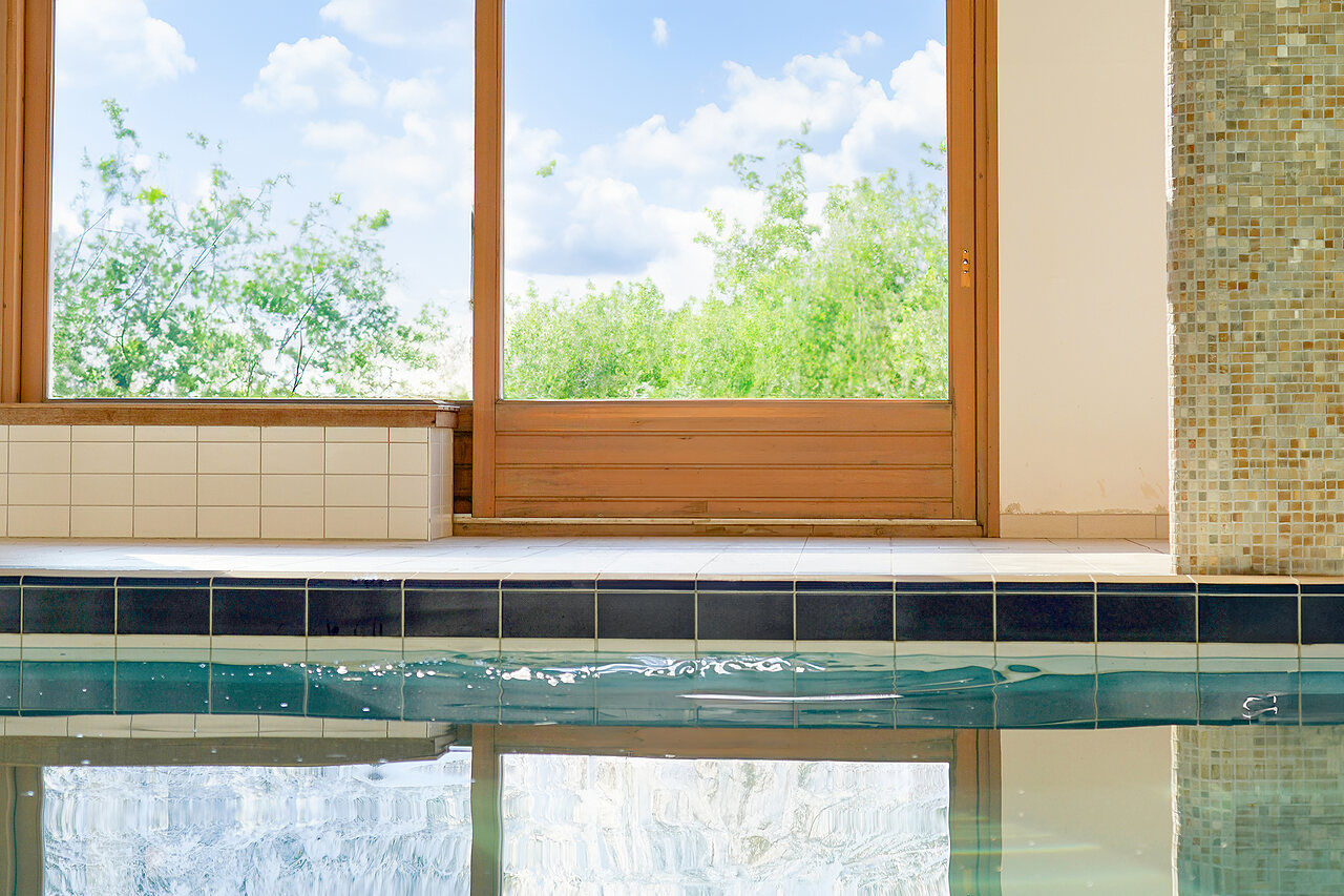 Indoor swimming pool edge with large windows overlooking nature at CLICOCHIC Alpes Lodges campsite in Pralognan la Vanoise (73).