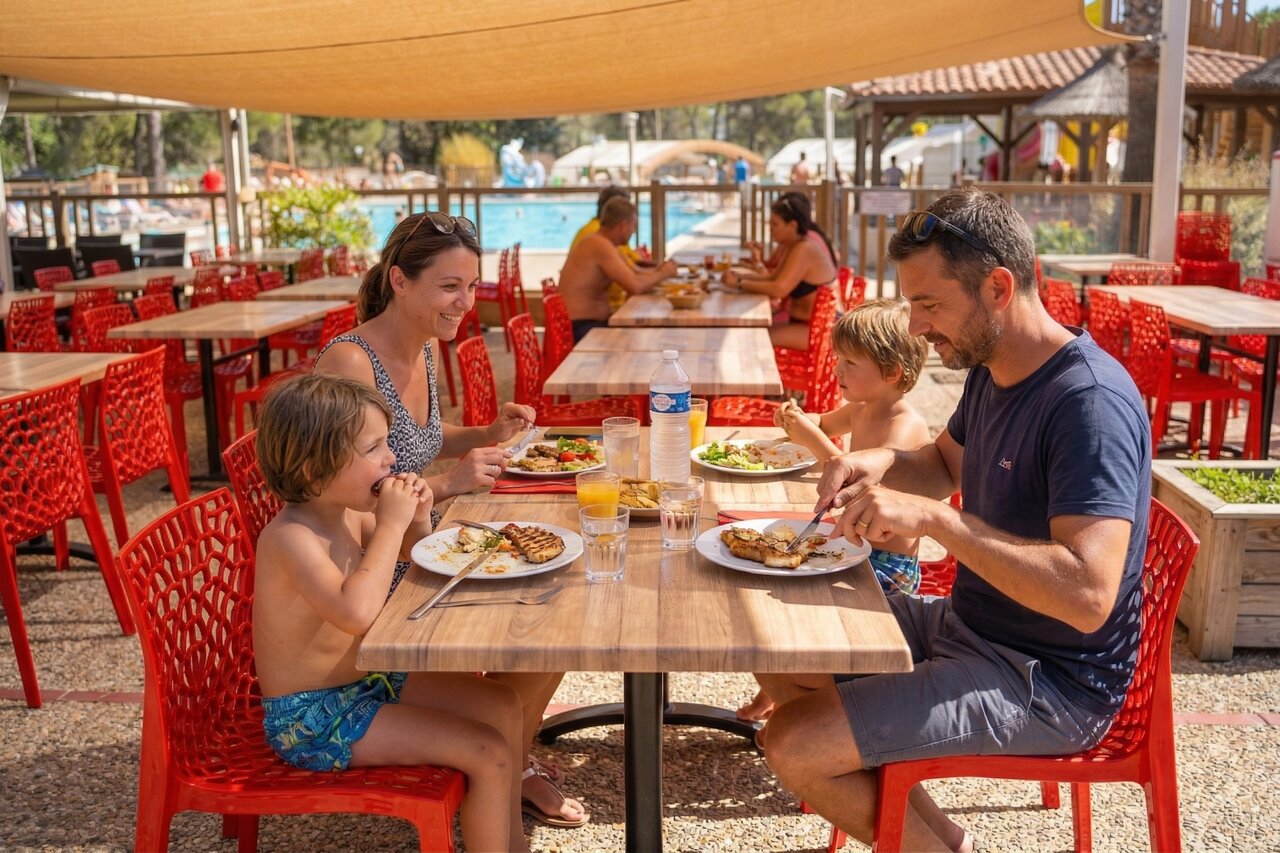 Familie isst im Au�enrestaurant nahe dem Pool auf Camping CAPFUN Arbois du Castellet in LE CASTELLET (83).