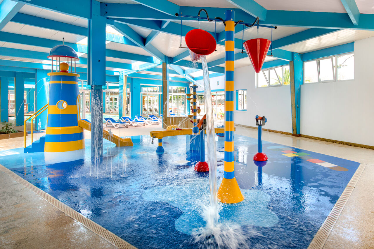 Indoor water play area with lighthouse slide and tipping buckets at LIBRANOO Naturiste Arnaoutchot campsite in Veille-Saint-Girons, Landes, France.