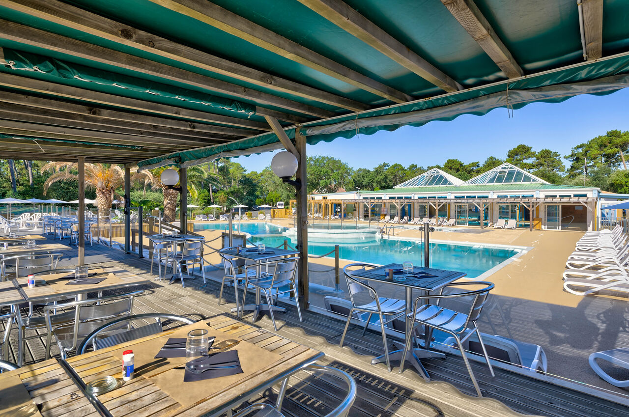 Shaded restaurant terrace overlooking the large outdoor swimming pool at LIBRANOO Naturiste Arnaoutchot campsite in Veille-Saint-Girons, Landes, France.
