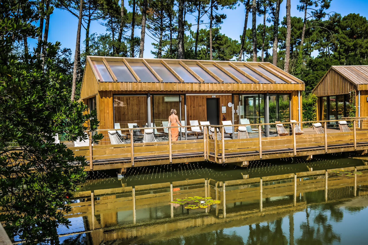 Modern spa building on stilts at LIBRANOO Naturiste Arnaoutchot campsite in Veille-Saint-Girons, Landes, France.