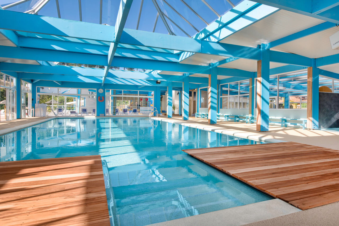 Bright indoor swimming pool with glass roof and wooden decks at LIBRANOO Naturiste Arnaoutchot campsite in Veille-Saint-Girons, Landes, France.