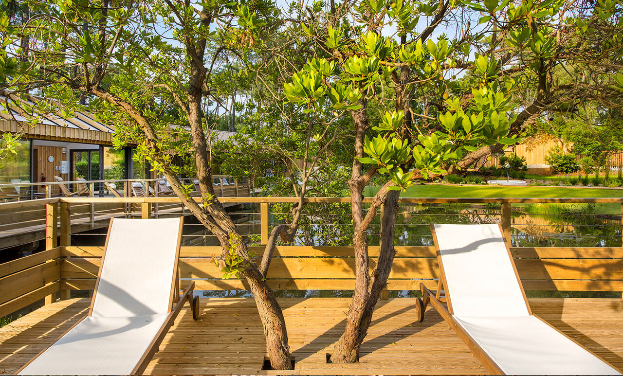Wooden deck, sun loungers and spa building at LIBRANOO Naturiste Arnaoutchot campsite in Veille-Saint-Girons, Landes, France.