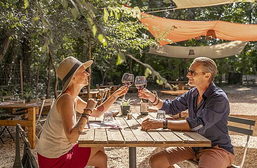 Paar stößt im schattigen Außenrestaurant des Campingplatzes CLICOCHIC Art de Vivre in Châteauneuf du Pape an.