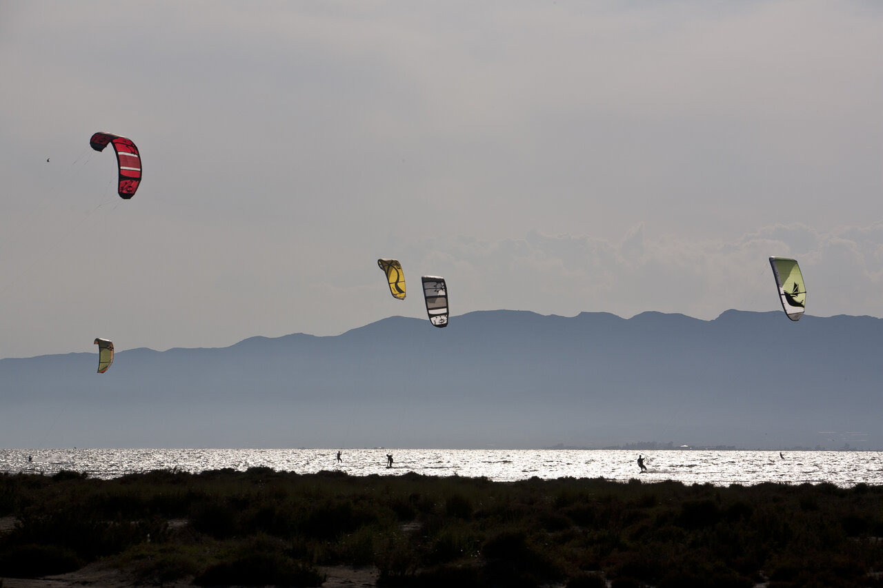 Kitesurfer auf glitzerndem Wasser mit Bergen am Camping CAPFUN Aube in Deltebre, Tarragona.