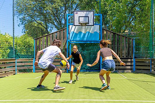 Young people playing basketball on multi-sport court at CLICOCHIC Baie de Cavalaire campsite.