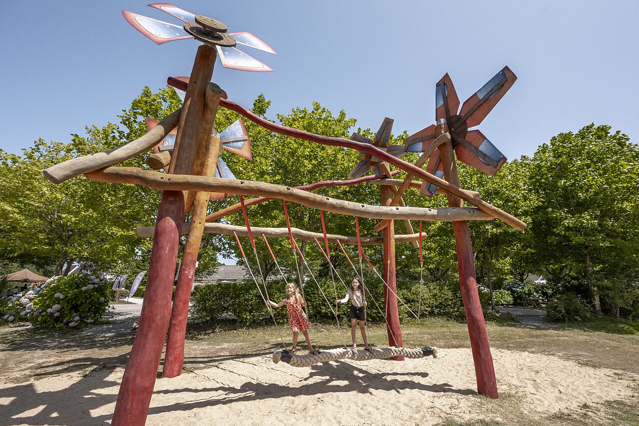 Riesige Holzschaukel mit zwei spielenden Kindern auf dem Campingplatz CLICOCHIC Baie de Douarnenez.
