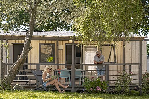 Modernes Mobilheim mit Terrasse, Paar entspannt auf Camping CLICOCHIC Baie de Douarnenez.