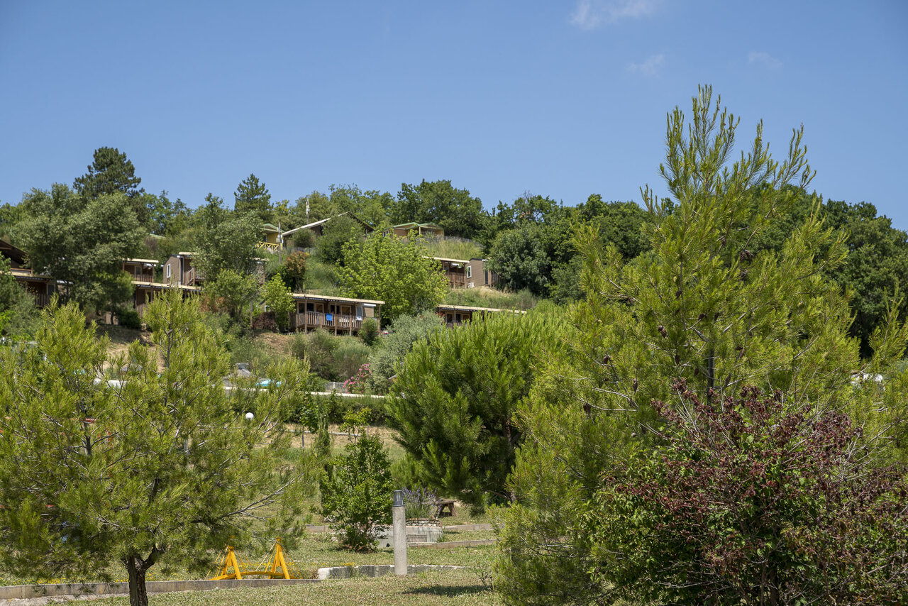 Wooden accommodations on green hillside at CLICOCHIC Bastets campsite in Marsanne (26).