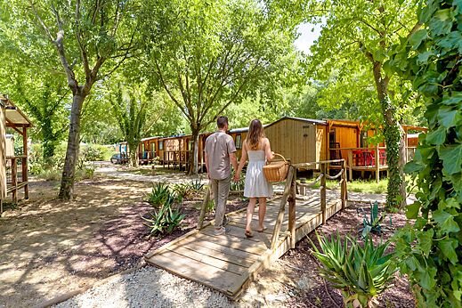Paar geht zu schattigen Mobilheimen auf Camping CAPFUN Bastide in Nîmes (30).