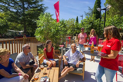 Buitenterras van de bar met gasten en serveerster op camping CAPFUN Bastide Nîmes (30).