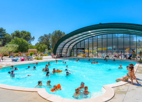 Large outdoor and indoor swimming pool with swimmers at CAPFUN Beauregard campsite in MORNAS (84).