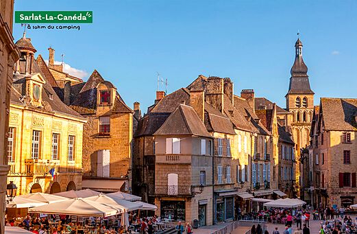 Belebter Platz in Sarlat-la-Canéda mit historischen Gebäuden und Restaurantterrassen.