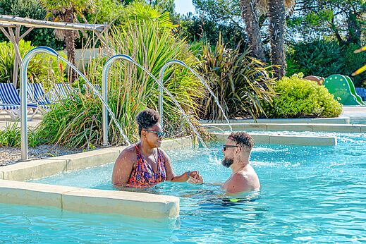 Swimming pool, water jets and smiling couple at VAGUES OCEANES Blancs Chênes campsite in LA TRANCHE SUR MER (85).