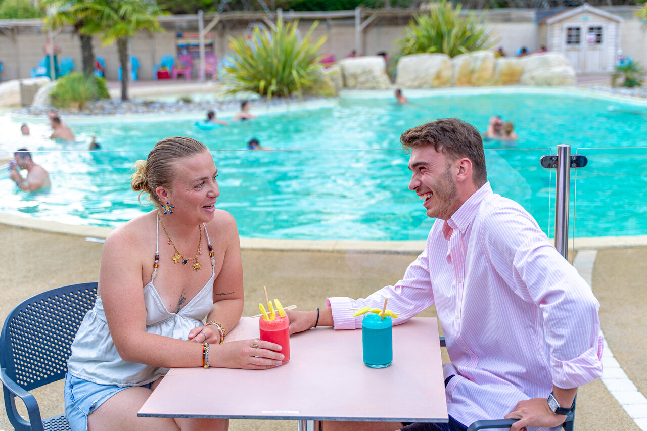 Lachendes Paar genie�t Cocktails am Pool auf dem Campingplatz VAGUES OCEANES Bois Joly in Saint-Jean-de-Monts (85).