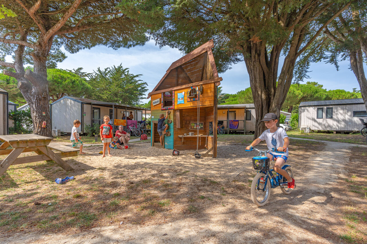 Speeltuin met houten huisje, kinderen en stacaravans op camping CAPFUN Bonne Etoile in BOIS PLAGE EN RE (17).