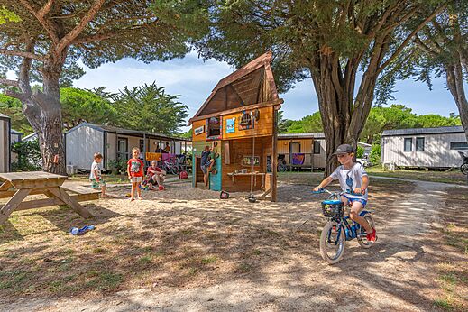 Spielplatz mit Holzstruktur und Kindern auf Fahrrad auf dem Campingplatz CAPFUN Bonne Etoile in BOIS PLAGE EN RE (17).
