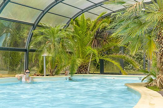 Überdachtes tropisches Schwimmbad mit Palmen und Badegästen auf dem Campingplatz CLICOCHIC Bordénéo Belle-Île-en-Mer in Le Palais (56).