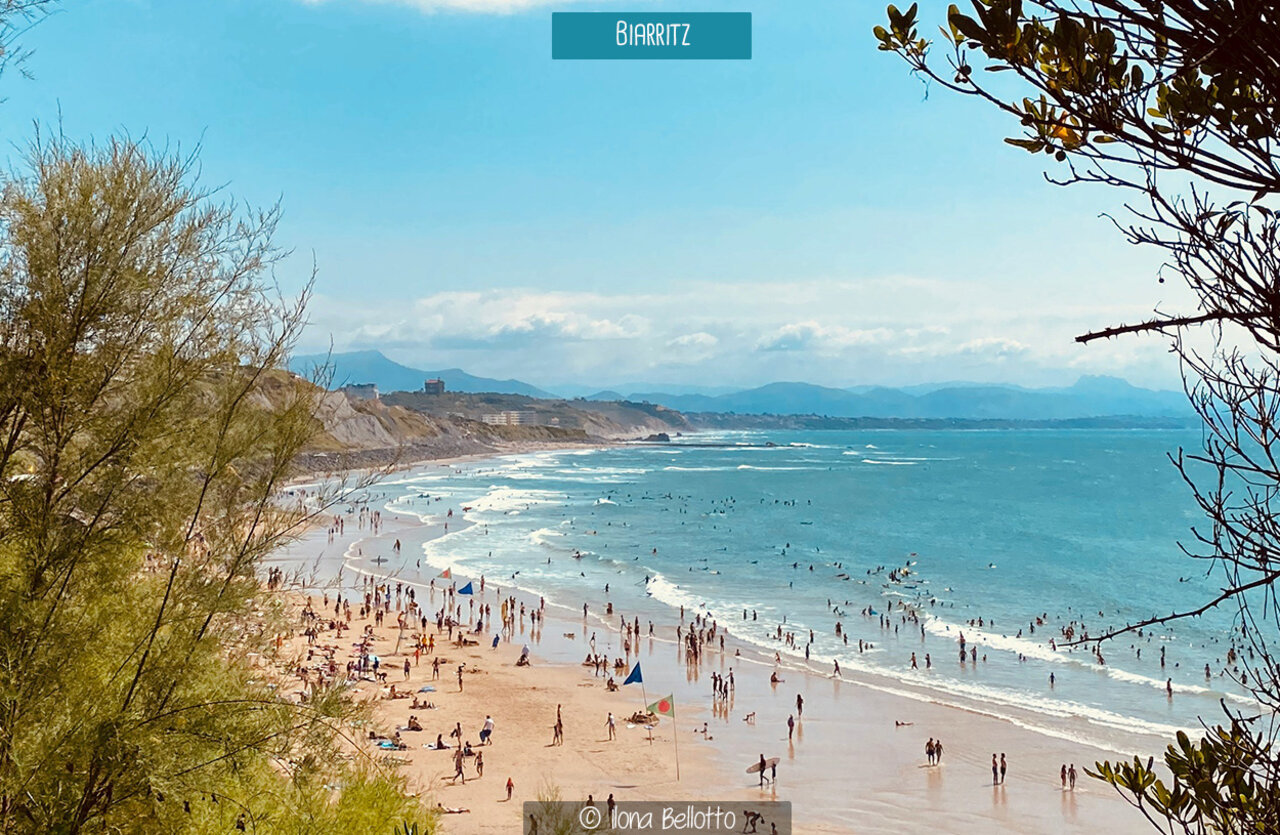 Lively beach in Biarritz, Basque Country, with swimmers and surfers under the sun.