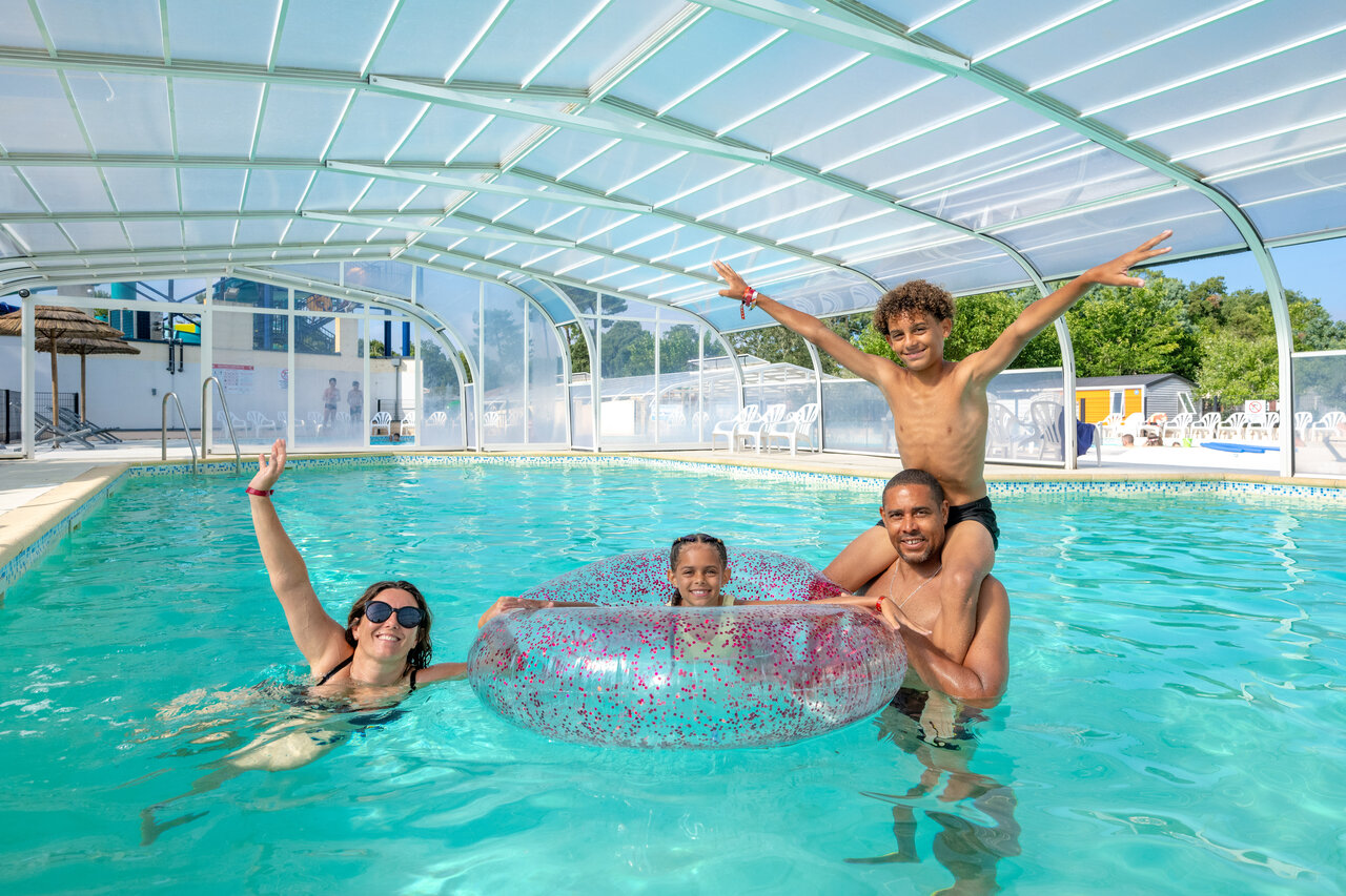 Smiling family enjoying the covered swimming pool at VAGUES OCEANES Boudigau campsite in LABENNE OCEAN (40).