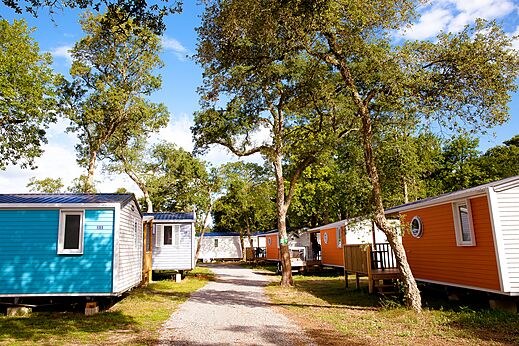 Bunte Mobilheime unter Bäumen auf dem Campingplatz VAGUES OCEANES Boudigau in LABENNE OCEAN (40).
