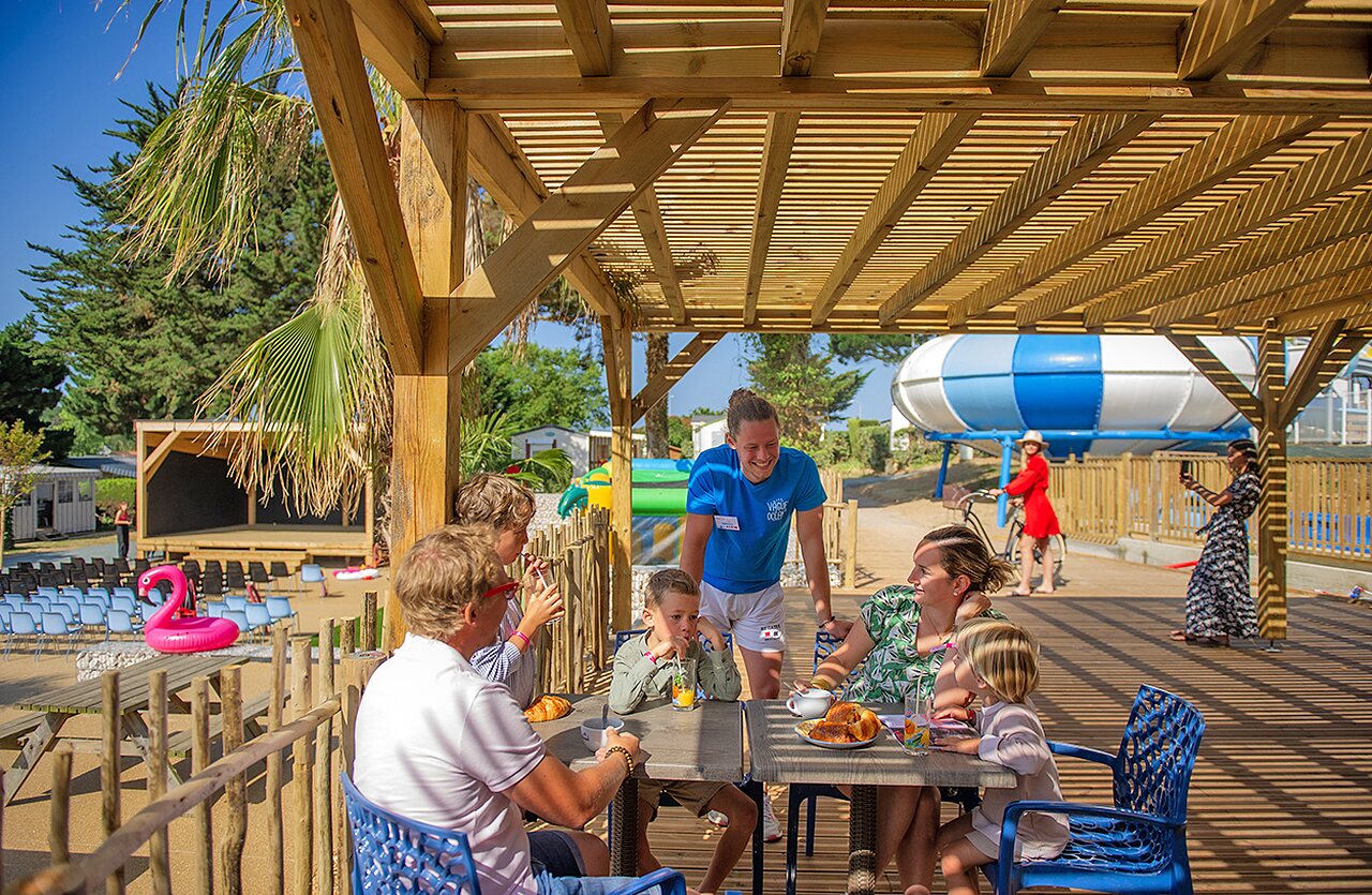 Familie fr�hst�ckt unter Pergola, Animateur, B�hne, Rutsche auf Camping CLICOCHIC Brandais in Brem sur Mer (85).