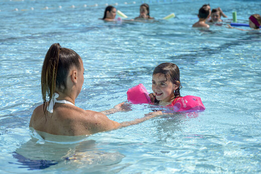 L�chelndes M�dchen mit Schwimmfl�geln und Erwachsener im Pool auf dem Campingplatz CAPFUN Breteche in Les Epesses (85).