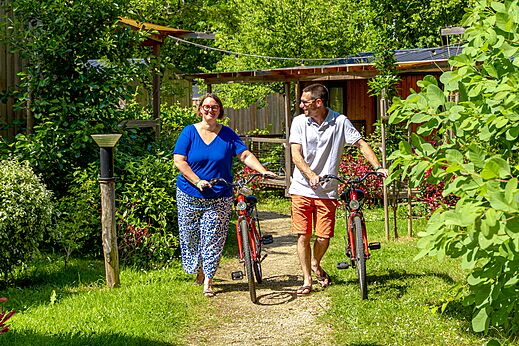 Couple walking with red bikes on green path at CAPFUN Breteche in Les Epesses (85).