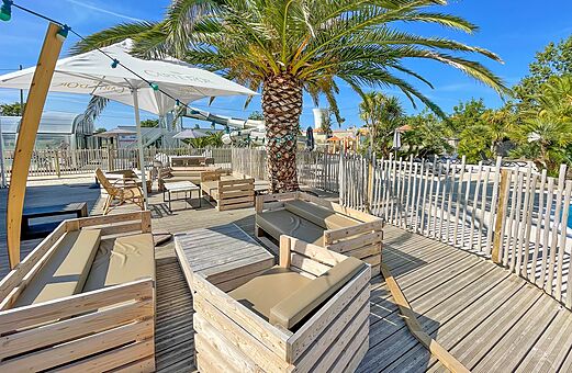 Outdoor bar terrace, wooden furniture, palm tree at camping CLICOCHIC Cabanes d Oléron.