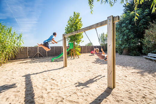 Zwei Kinder spielen auf Schaukeln auf dem Spielplatz des Campingplatzes CLICOCHIC Camp du Soleil in Ars-en-R� (17).