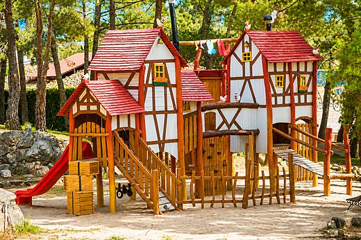 Grote houten speeltuin met glijbaan en bruggen op camping CAPFUN El Canto La Gallina in Valdemaqueda (Madrid).