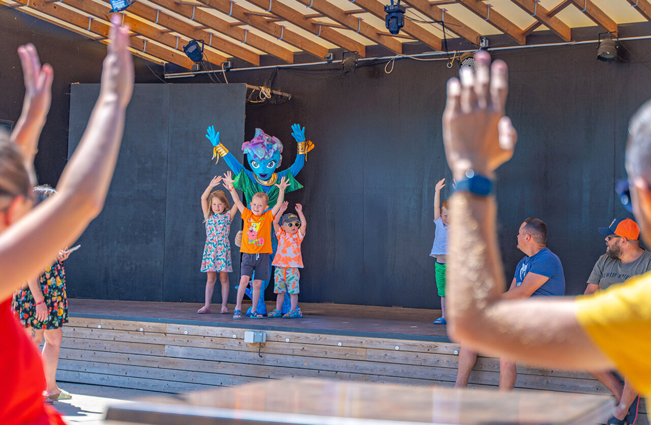 Kinderanimatie met mascotte op podium bij camping VAGUES OCEANES Domaine les Charmilles.