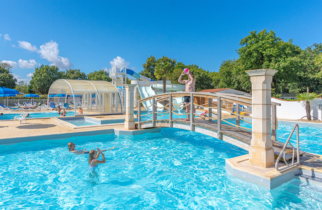 Buitenzwembad, waterglijbanen en decoratieve brug op camping VAGUES OCEANES Domaine les Charmilles in Saint-Laurent-de-la-Pr�e (17).