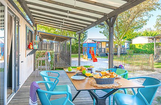 Terrasse eines Mobilheims mit Fr�hst�ck und Spielplatz auf dem Campingplatz VAGUES OCEANES Domaine les Charmilles in Saint-Laurent-de-la-Pr�e (17).
