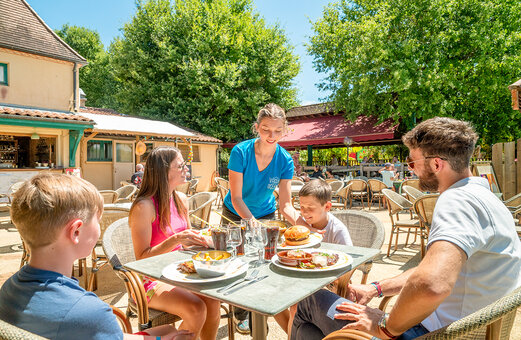 Familie isst auf der Restaurantterrasse auf dem Campingplatz VAGUES OCEANES Chataigneraie in Prats-de-Carlux.