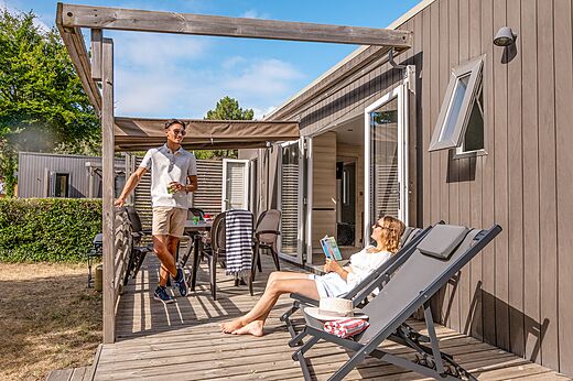 Modernes Mobilheim mit Holzterrasse und Paar auf dem Campingplatz CLICOCHIC Chouans in SAINT HILAIRE DE RIEZ (85).