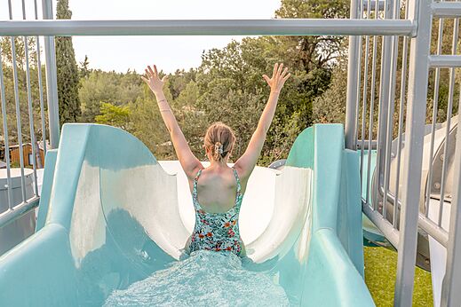 Frau auf Wasserrutsche, Arme erhoben, auf Campingplatz CLICOCHIC Commanderie in Rustiques.