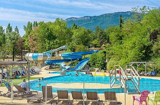 Piscine extérieure avec toboggans aquatiques et chaises au camping CLICOCHIC Couriou à Recoubeau-Jansac (26).