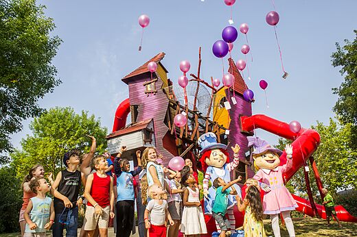 Kinder und Maskottchen vor farbenfrohem Spielplatz mit Rutschen auf Camping CAPFUN Curty's in Jard sur Mer (85).