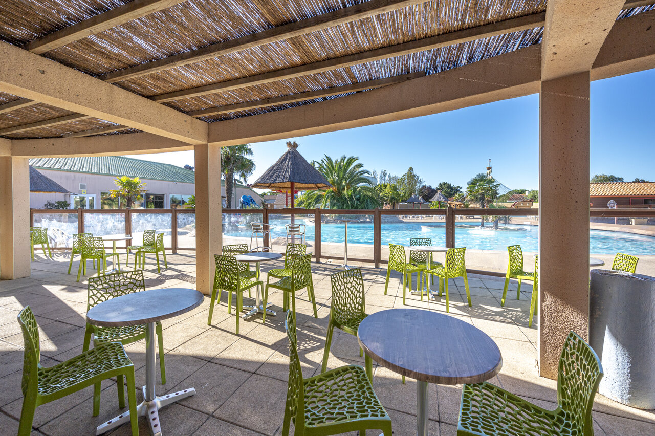 Schattige Barterrasse mit Tischen und gr�nen St�hlen, am Pool, auf dem Campingplatz CAPFUN Dauphins Bleus in GIVRAND (85).