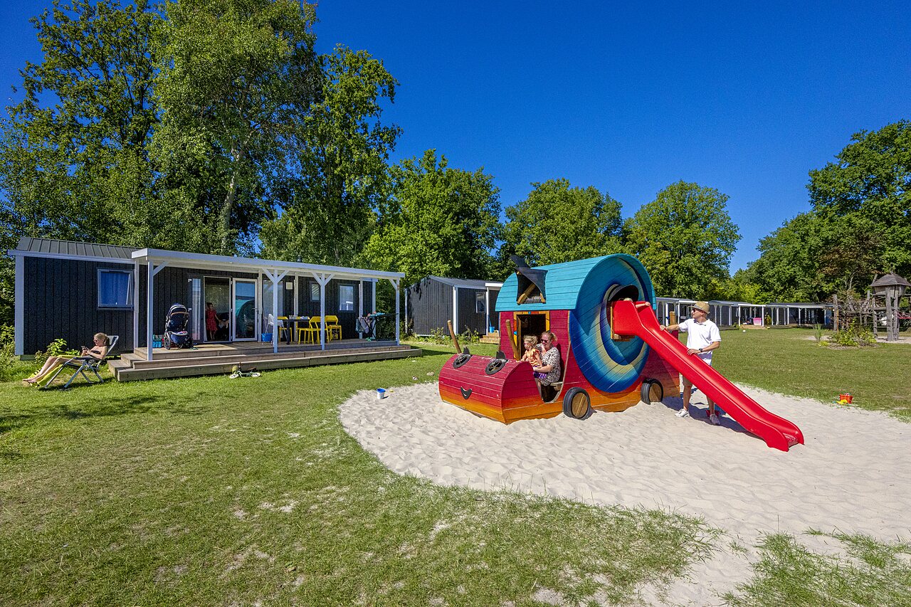Bunter Spielplatz mit Rutsche und Mobilheimen auf dem Campingplatz CAPFUN De Belten in Rheeze.
