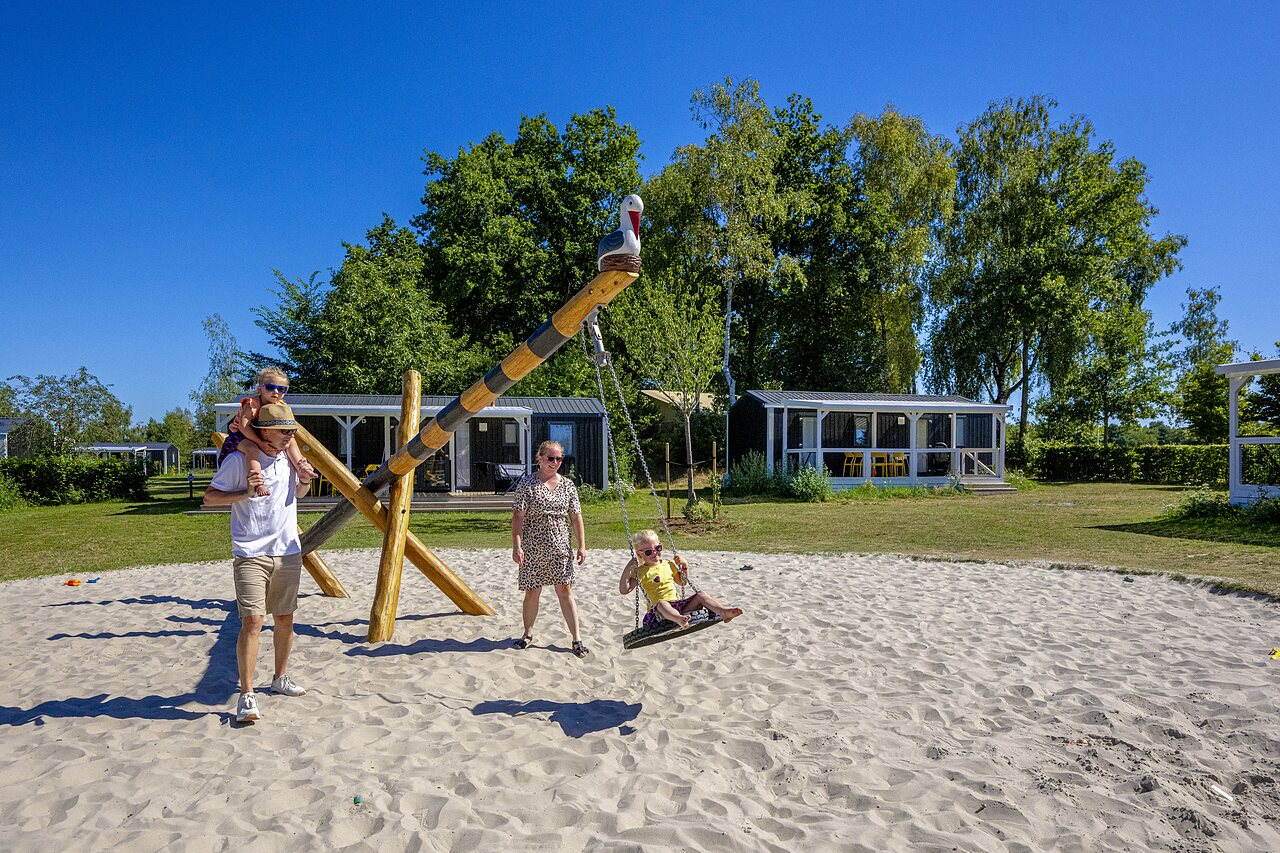 Sandspielplatz mit Schaukel und Familie, Mobilheime auf dem Campingplatz CAPFUN De Belten in Rheeze.