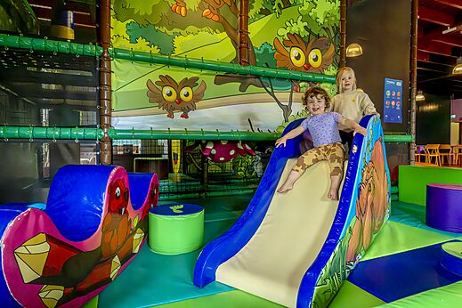 Lachende Kinder auf einer Rutsche im Indoor-Spielplatz auf dem Campingplatz CAPFUN De Belten in Rheeze.