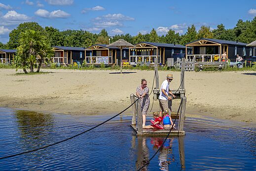Familie auf Floß zieht Seil, Strand und Mobilheime auf Camping CAPFUN De Belten in Rheeze.