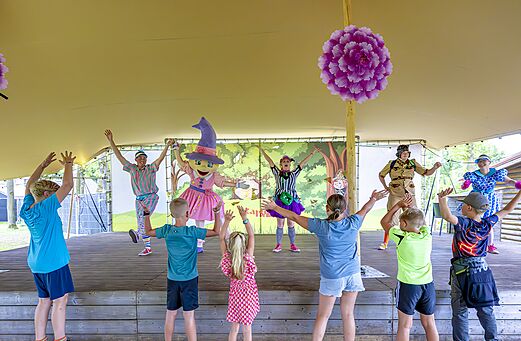 Kinder und Animateure in Kostümen bei einer Animation auf der Bühne auf dem Campingplatz CAPFUN De Belten in Rheeze.
