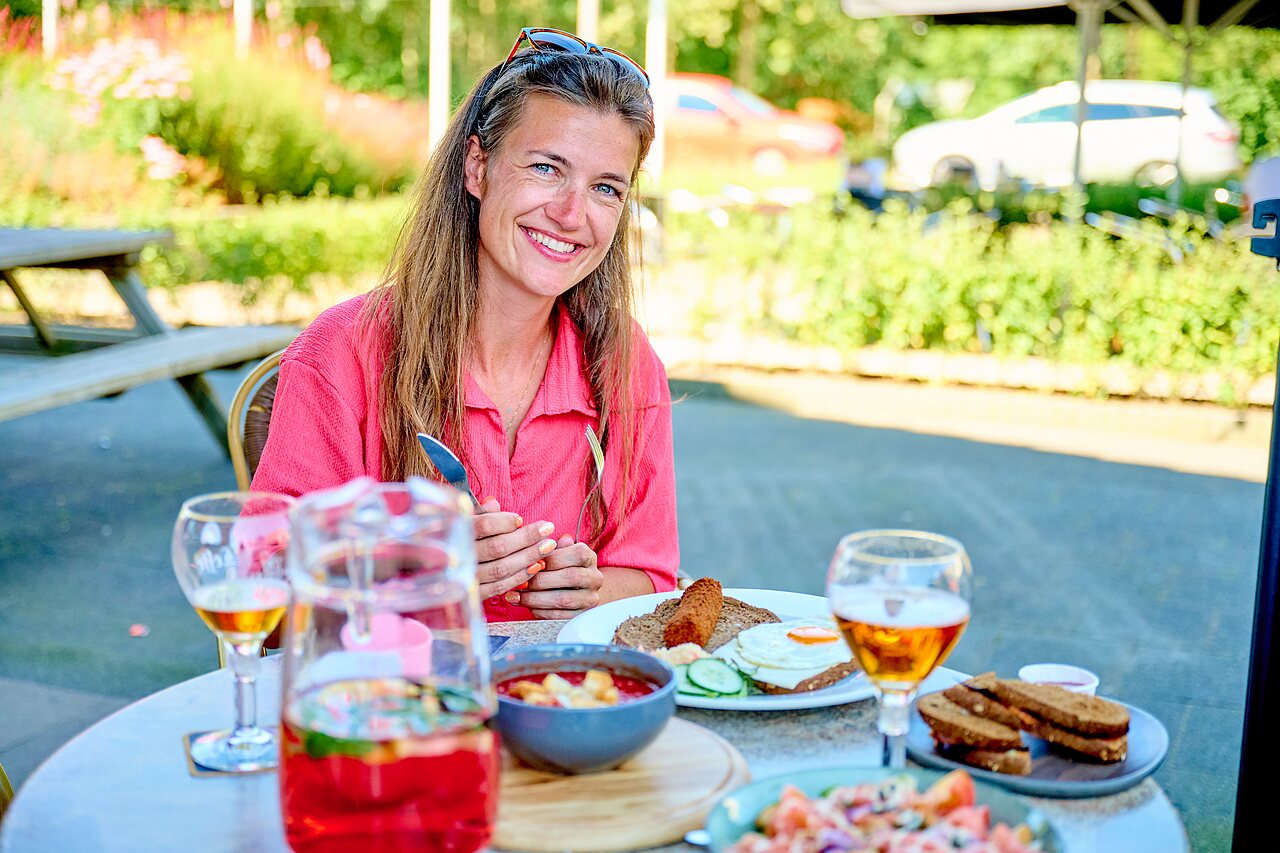 L�chelnde Frau genie�t Mittagessen auf Terrasse, Camping CAPFUN De Eikenhof in Paasloo/Oldemarkt.
