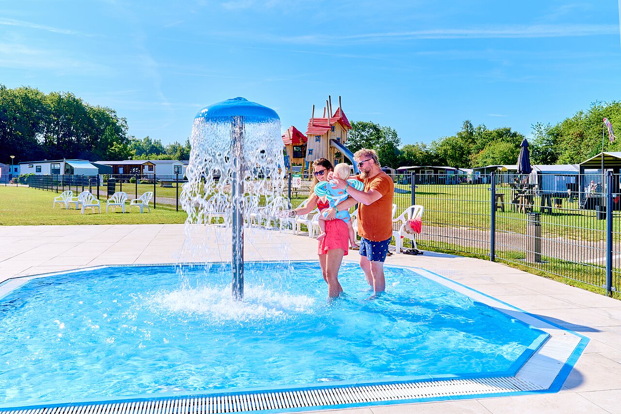 Familie mit Baby im Planschbecken mit Wasserpilz, Spielplatz auf dem Campingplatz CAPFUN De Eikenhof in Paasloo/Oldemarkt.