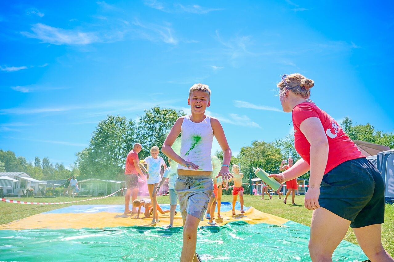 Kinder und Animateur auf farbiger Wasserrutsche im Camping CAPFUN De Eikenhof.